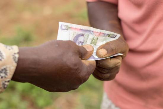 Someone handing a Kenyan paper currency to someone else