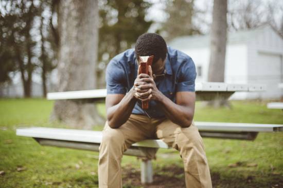 A man sitting on a park bench and praying with his Bible in his hands