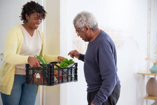 A young woman holding out a crate of vegetables to her grandfather