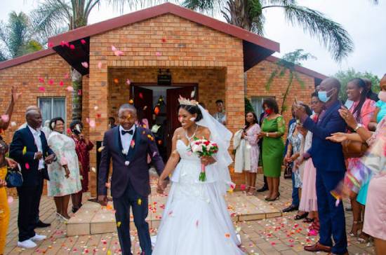 A newly-married couple leaving a church with friends and family tossing flower petals in their path