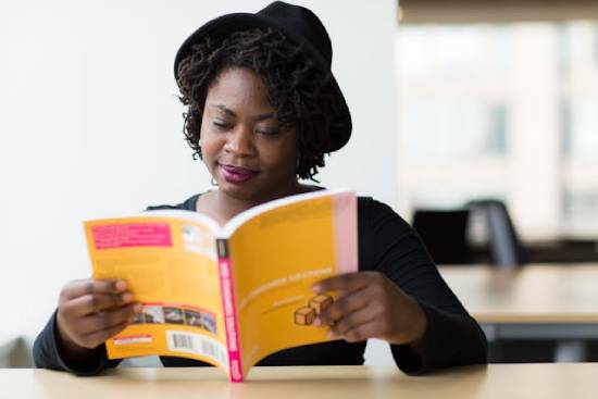 A woman in a black long-sleeved blouse reading a yellow-covered book to learn more about contentment and stewardship.