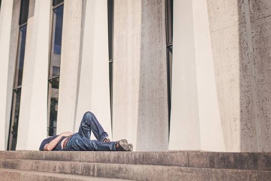 A drained and fatigued man lying flat on a pavement.
