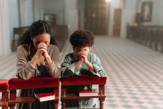 A Mother and a Son Kneeling in Prayer A mother kneeling in prayer with her son as a way instilling faith and devotional practices in his life.