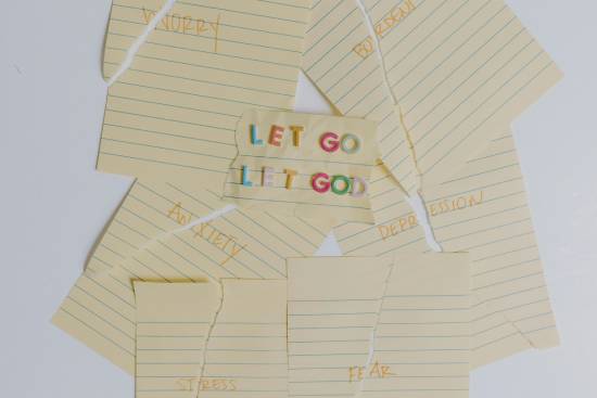 Let Go, Let God written in bold letters surrounded by ripped papers with stressful feelings written on them Torn notebook papers describing struggles like depression and anxiety arranged around a central paper with the message to 'let go and let God' deal with these problems