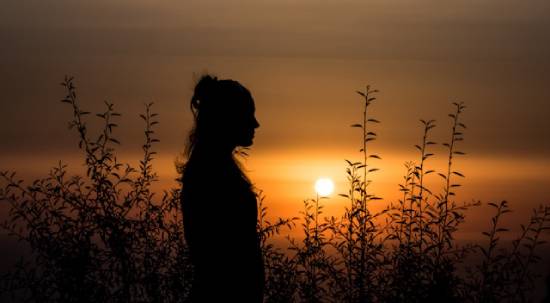 Silhoutte of a woman meditating on emotional healing at dusk.