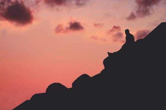 A silhouette of a man resting on a mountain peak before continuing with his goal of climbing to the top.