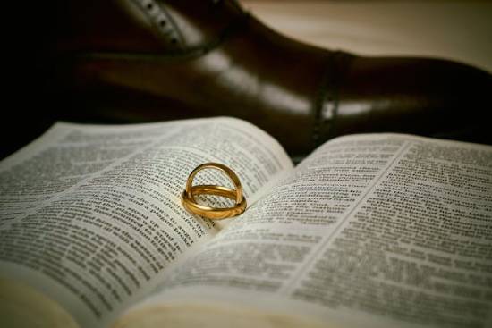 Wedding Rings on an Open Bible Next to a Shoe Golden wedding rings placed inside an open Bible next to a black leather shoe.