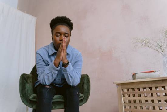 An afro-haired woman sitting on a chair praying to God for clarity in some consequential decisions she needs to make