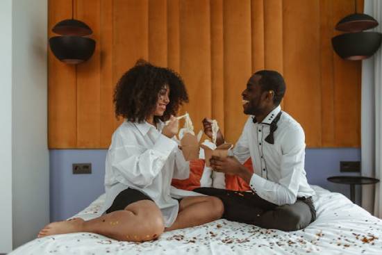 A happy couple eating snacks in the bedroom as they engage in a conversation.