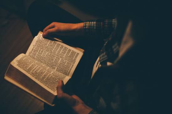 A Person Reading the Bible A person reading the Bible under light in a room.