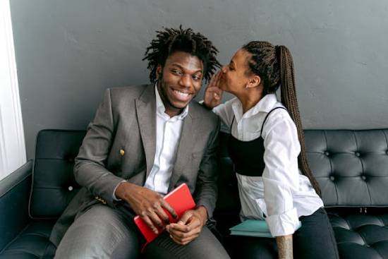 A Woman Whispering to a Man A happy woman whispering to a man in dreadlocks and a grey suit.