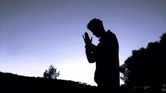 A silhouette of of man kneeling in prayer in the evening.