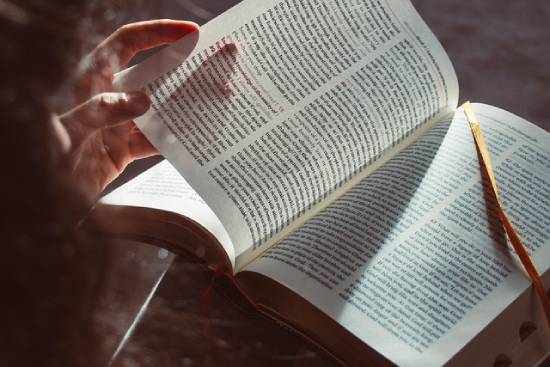 A person's hand flipping the pages of a Bible.