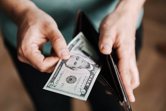 A generous person removing five dollars note from his wallet ready to give to the needy.