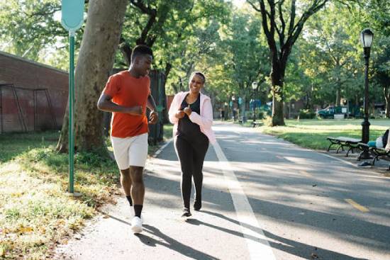 Man and a Woman Running A man a red t-shirt and white shorts and a woman in black and pink jumper running at the park.