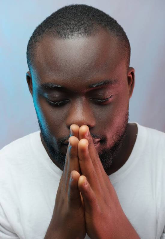 A Man Focused on Prayer A man in a white roun-neck t-shirt with hands put together focused on prayer.