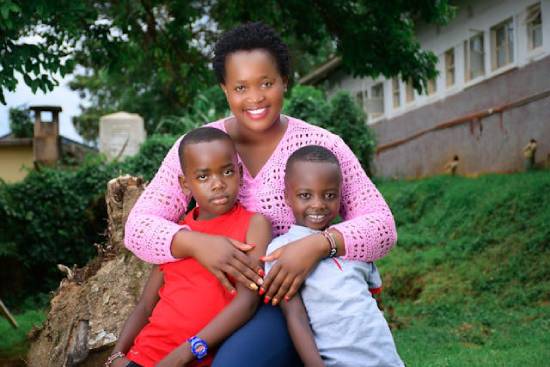 A smiling mother in a pink knitted top embracing her two sons.