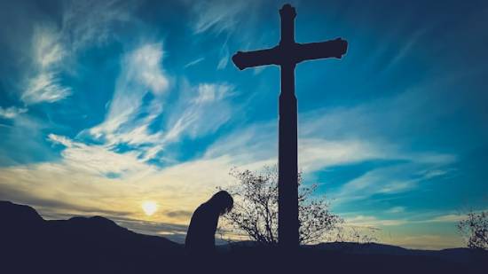A Silhouette of a Repentant Person Silhouette of a repentant person kneeling in prayer in front of a cross.