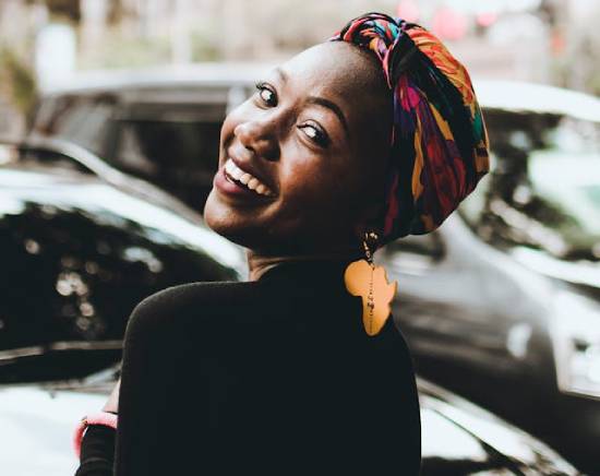 A smiling woman in a multi-coloured head wrap and Africa-shaped earrings.