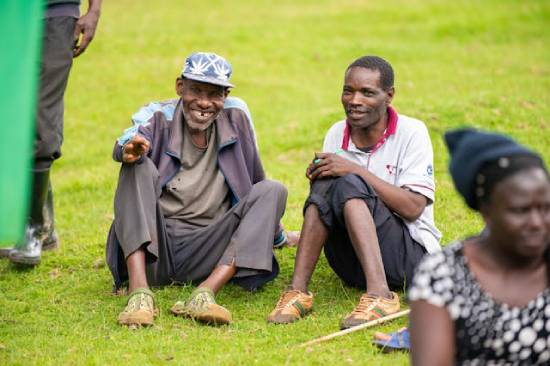 Two adult men smiling while having a talk on parenting, seated on a lawn.