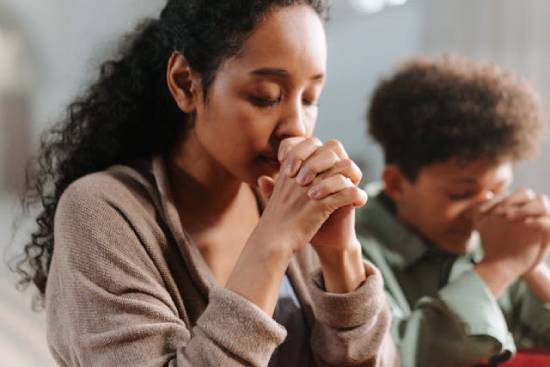 Praying With a Friend A young woman in a black sweater praying with a friend.