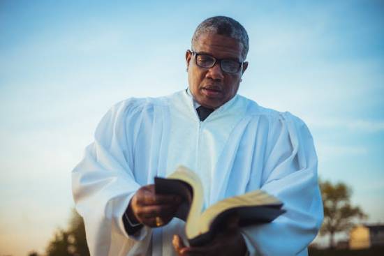 A clergyman opening the Bible in eyeglasses and white sacerdotal robe opening the bible.