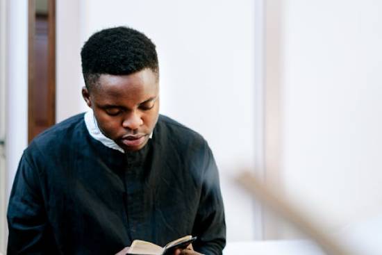 A Man Reading the Bible A close-up shot of a man in black sacerdotal robe reading the Bible.