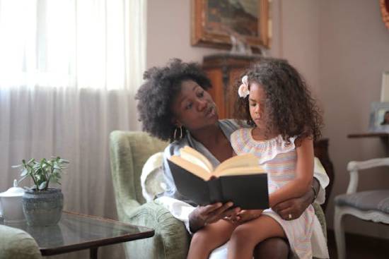 Mother Giving Daughter Scripture Affirmations Mother carrying her daughter on her lap and reading to her Scripture affirmations to remind her of her identity.