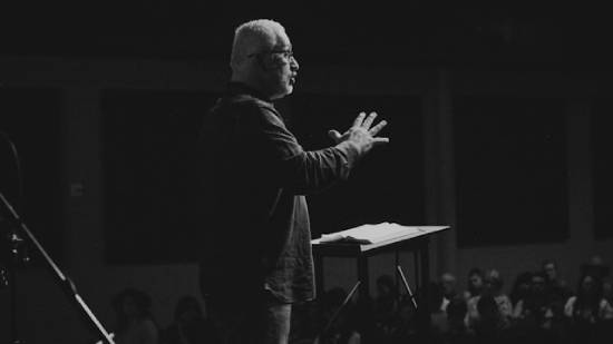 A pastor standing on the podium preaching with his open Bible on the podium.