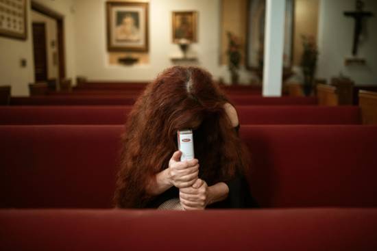A woman holding her Bible and praying with head bowed while sitting alone on a red pew.
