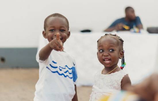 Siblings Standing Together A boy in a white shirt with blue strips standing next to a girl in a white dress.