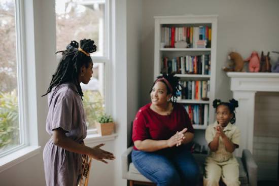 A happy mother in denim trousers and wine-red top bonding with daughters in the living room.