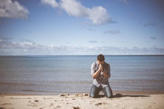 Praying and Fasting A man kneeling in prayer by the ocean.
