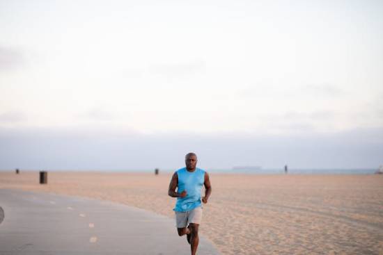 A man in a blue top and grey shorts running in a tarmacked track.