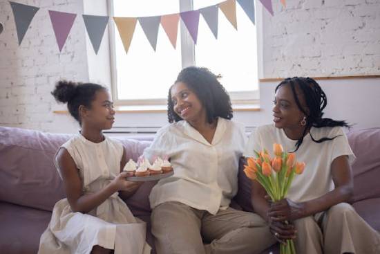 Family Celebration A mother celebrating with two daughters who have brought flowers and cakes.