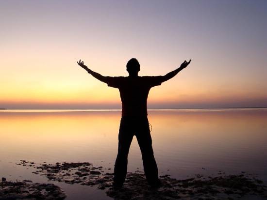 Silhouette of a man lifting his arm in prayer during the golden hour.