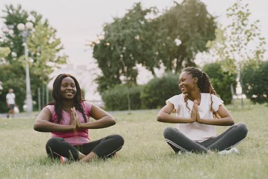Two women sitting on a grassy field doing yoga.