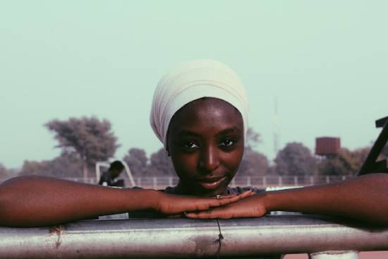 A woman wearing a white headwrap resting her arms and head on metallic fence.