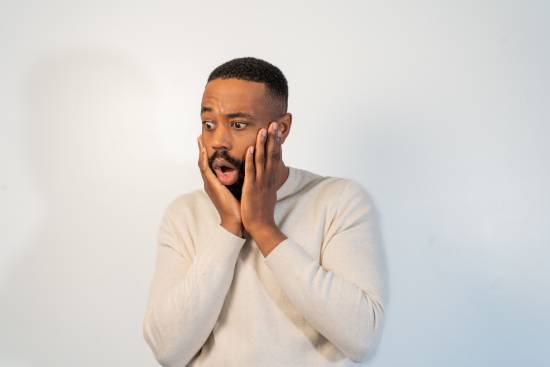 A Shocked Man A shocked man in a cream long-sleeved top holding his chin.
